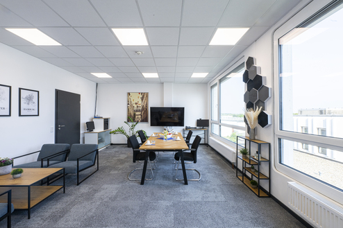 Moderne Büroräume mit Tisch, Stühlen, Pflanzen und großen Fenstern, die auf die Umgebung blicken.