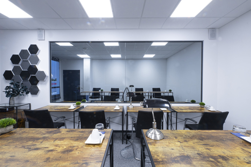 Blick auf einen modernen Besprechungsraum mit Tischen, Stühlen, Pflanzen und einer großen Glaswand.