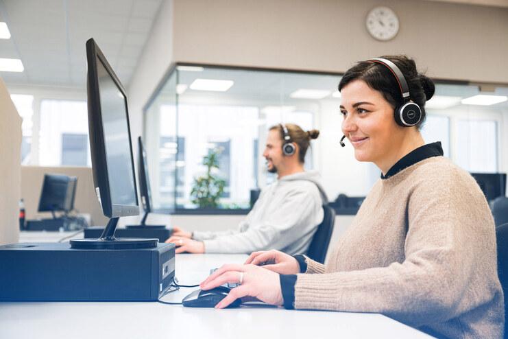 Zwei Personen arbeiten an Computern in einem modernen Büro, beide tragen Headsets und interagieren am Arbeitsplatz.