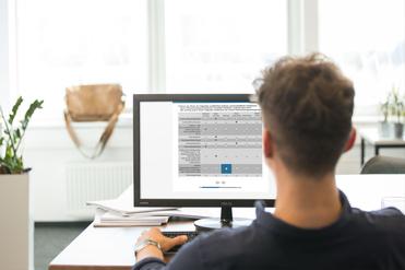 Mann sitzt am Tisch und betrachtet eine Computeranzeige mit Bewertungskriterien auf einem Monitor.