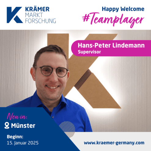 Mann mit Brille in blauer Hemd lächelt vor einer beleuchteten K-Form und Firmenlogo von Krämer Marktforschung.