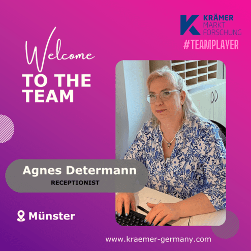 Frau mit Brille und blauer Bluse sitzt an einem Schreibtisch und arbeitet am Computer in einem Büro.