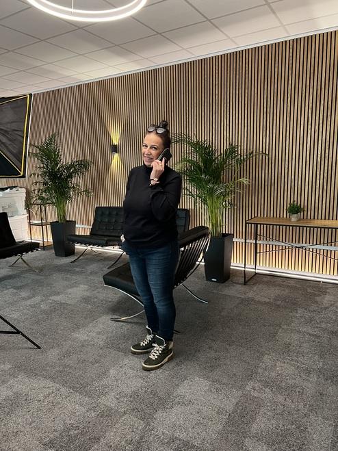 Frau mit Telefon in einem modernen Raum, umgeben von Pflanzen und designorientierten Möbeln.