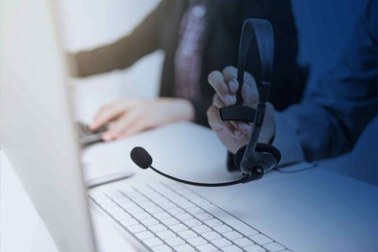 Nahaufnahme eines Headsets, während eine Hand auf einer Computer-Tastatur tippt. Schreibtisch in sanften Farbtönen.