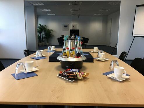 Konferenzraum mit einem runden Tisch im Zentrum, umgeben von Stühlen und dekoriert mit Getränken und Snacks.