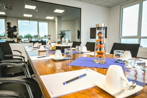 Konferenzraum mit Holzttisch, Wasserkaraffe mit Fr&uuml;chten und Schreibutensilien auf blauer Tischdecke.